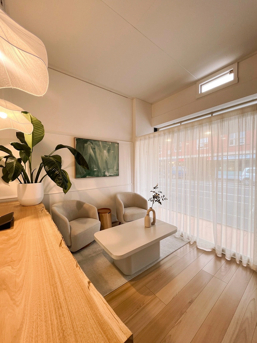 Santal reception area with cream boucle chairs, sheer curtains, timber floors, large-leafed plants and the live-edge timber counter
